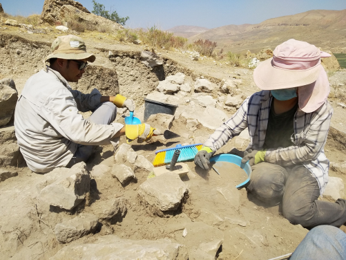 Two HKU students uncover the collapsed top of an ancient wall at the Vedi Fortress, with the mountains of the Vedi River valley visible in the background.